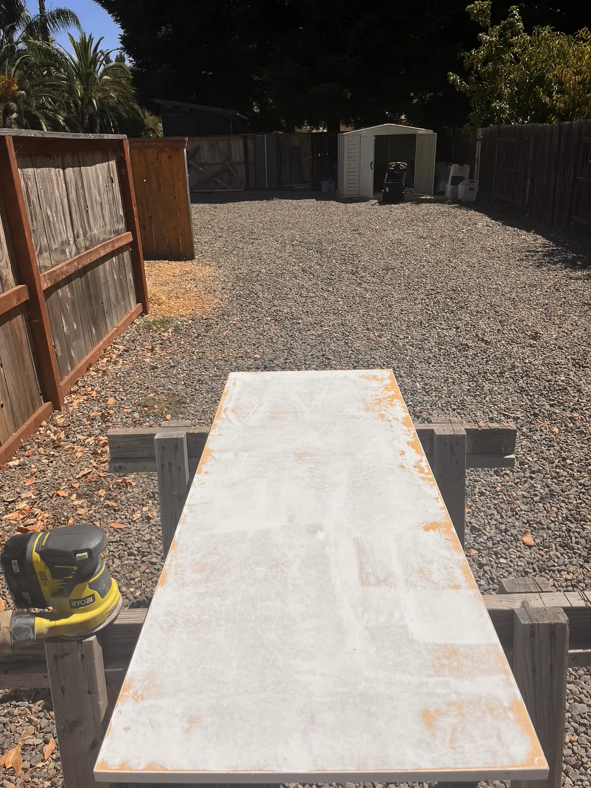 A wooden outdoor work table with a power sander during a refinishing project