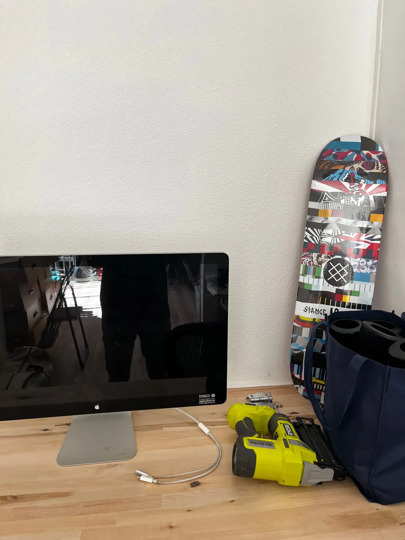 An iMac, skateboard, and power tool arranged on a workbench